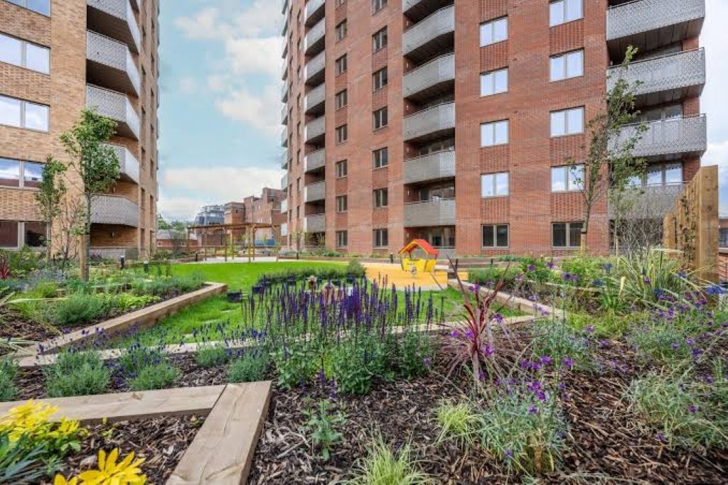 A multi-story residential building with balconies, a landscaped garden with various plants, and a playground area.