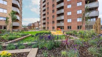 A multi-story residential building with balconies, a landscaped garden with various plants, and a playground area.