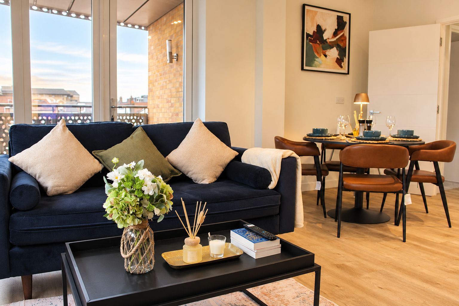 Een moderne woonkamer met een donkerblauwe bank, een salontafel en een eethoek met een tafel gedekt voor twee personen.