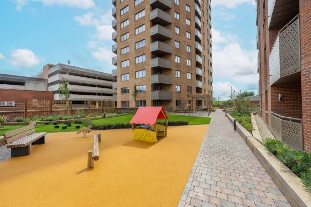 A multi-story residential building with balconies, a paved walkway, and a small play area with a red-roofed structure.