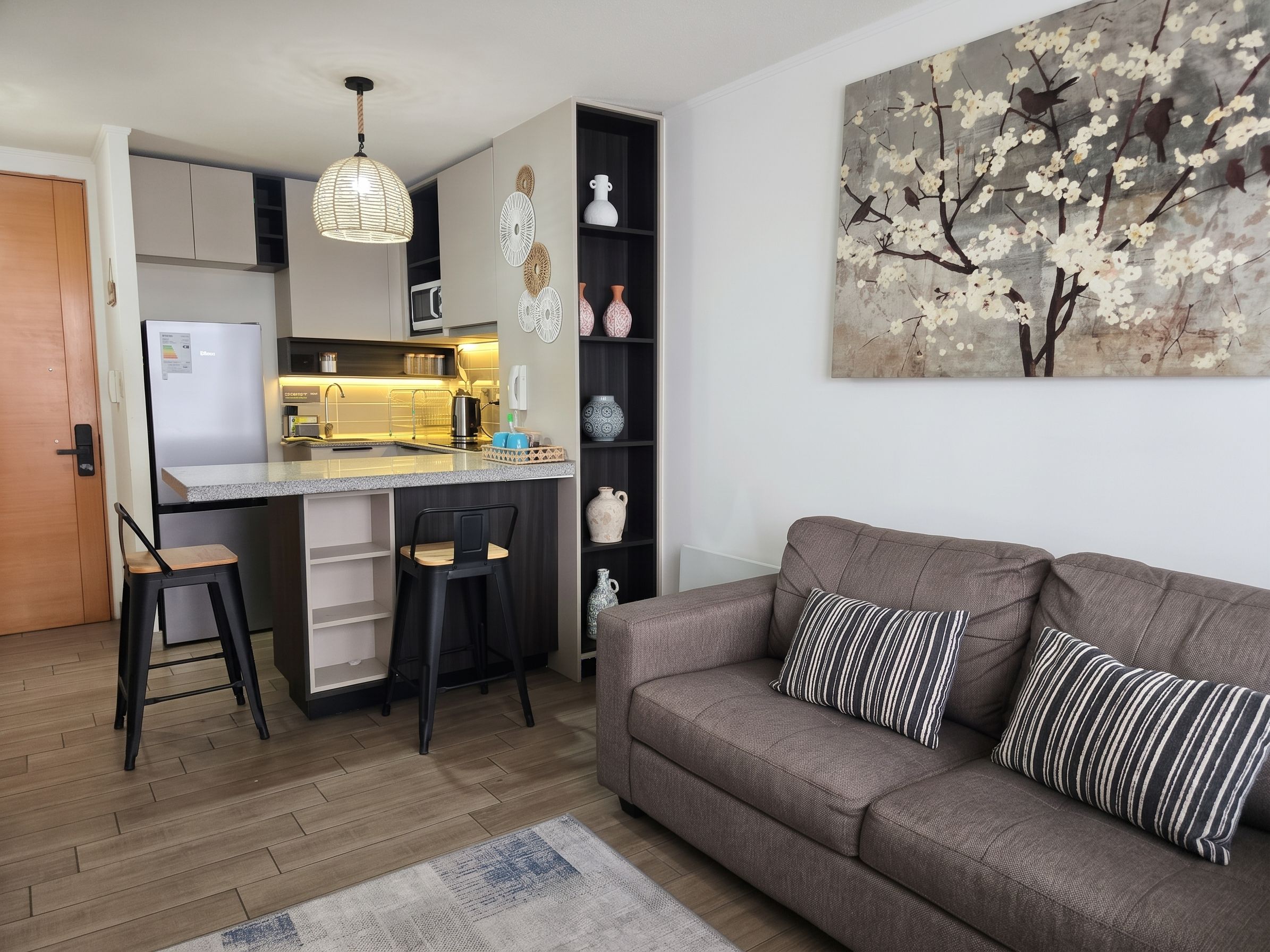 Una cocina moderna con microondas integrado, un comedor con una silla de madera y una sala de estar con sofá y almohadas a rayas.