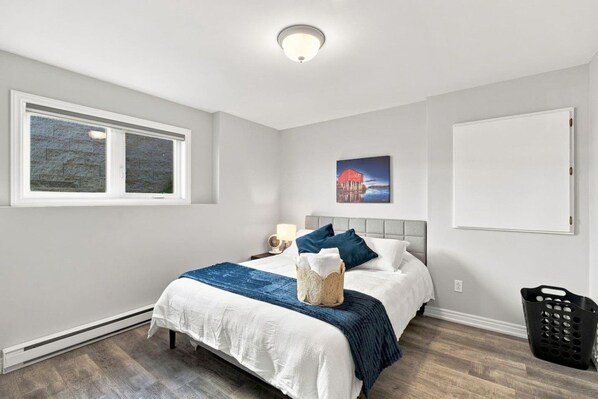 A bedroom with a bed, a nightstand, a lamp, a picture on the wall, and a window.