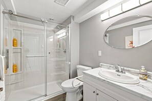 A modern bathroom with a glass-enclosed shower, a white toilet, a marble sink, and a mirror with a round frame.