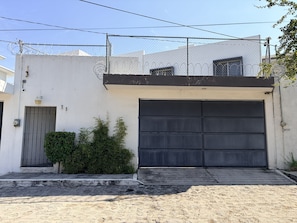 Un edificio residencial con un gran portón de garaje, acceso mediante portones y una pequeña zona ajardinada.