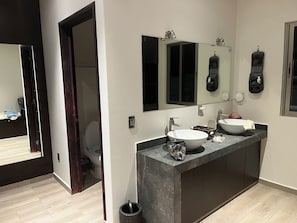 Un baño moderno con un amplio tocador, un lavabo y un espejo. Se ve un inodoro en la habitación contigua.