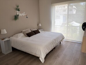 Un dormitorio con una cama, dos mesitas de noche, una ventana y vistas a edificios.