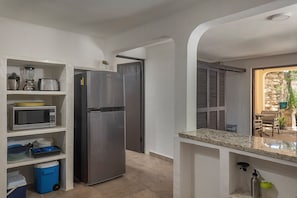 A compact kitchen with a refrigerator, microwave, and a small dining area with a stone wall and a potted plant. - Casita Cuna (Puerto Morelos)