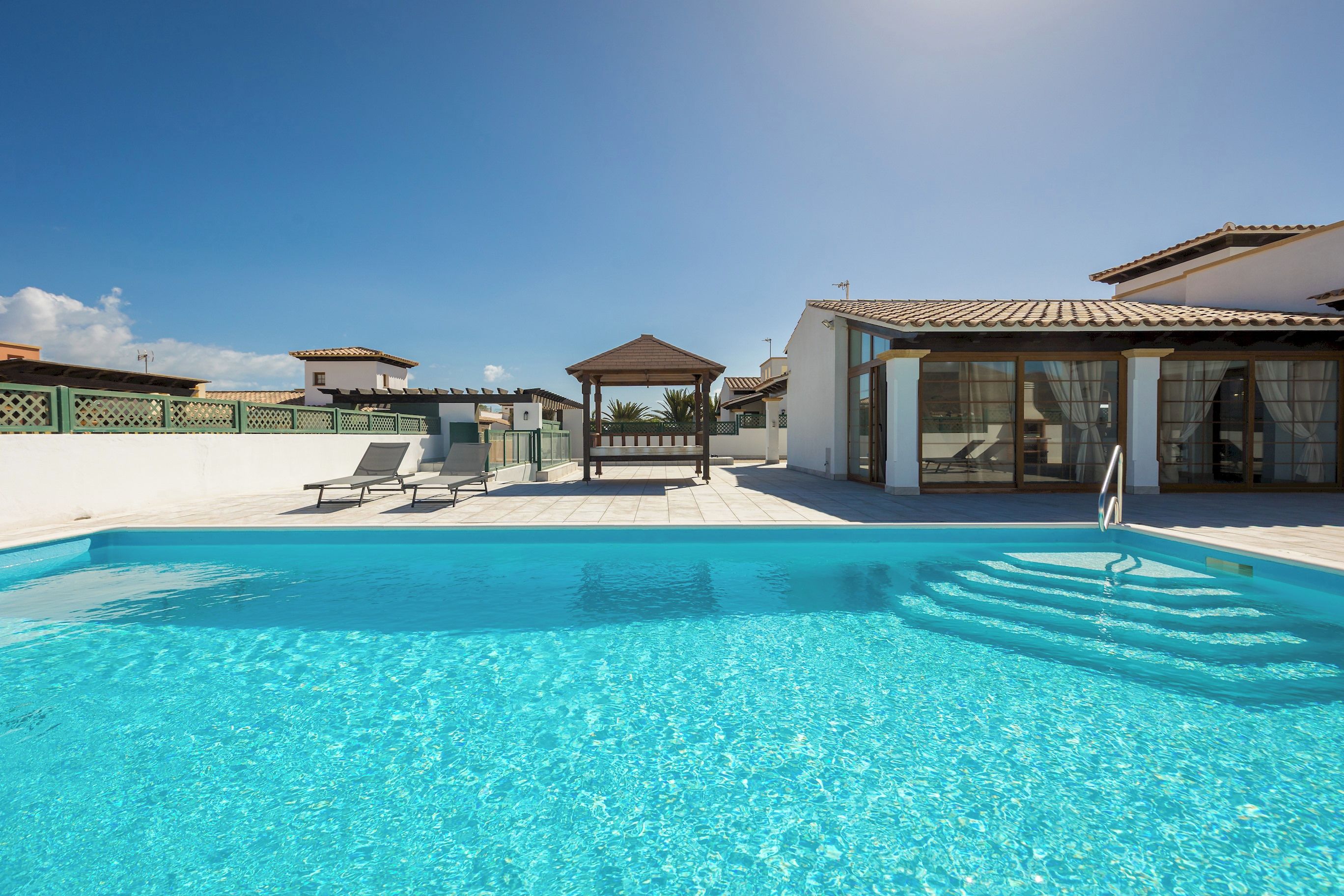 Ein klares, blaues Schwimmbecken mit Liegestühlen und einer Laube in einer Resort-Umgebung.
