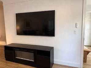 Un téléviseur à écran plat fixé à un mur blanc, un meuble noir pour appareils électroniques en dessous, et une porte blanche sur la droite.