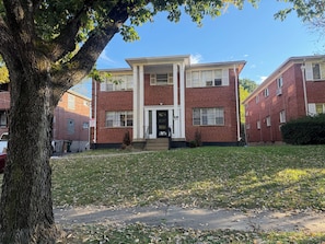 A two-story brick building with a front porch and a small front yard. - Updated 2BR Extended Stay with Parking and On-Site Laundry (Cincinnati)