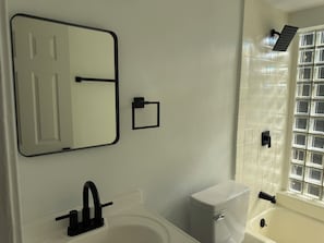 A bathroom with a white sink, a toilet, a mirror, and a shower. - Updated 2BR Extended Stay with Parking and On-Site Laundry (Cincinnati)