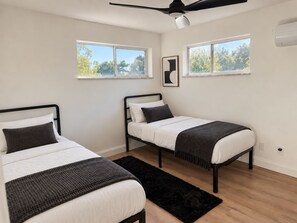 A bedroom with two beds, a ceiling fan, and two windows with a view of trees. - Updated 2BR Extended Stay with Parking and On-Site Laundry (Cincinnati)