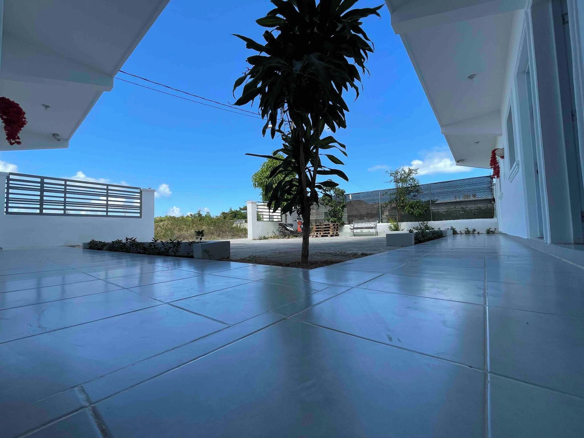 A spacious outdoor area with a tiled floor, a small tree, and a clear blue sky.