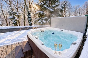 Un jacuzzi con dos copas de champán, rodeado de árboles cubiertos de nieve y una terraza de madera.