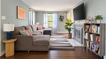 A living room with a sectional sofa, a coffee table, a bookshelf, a fireplace, and a television.