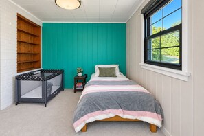 Un dormitorio con una cama, una ventana, una cuna y una estantería.