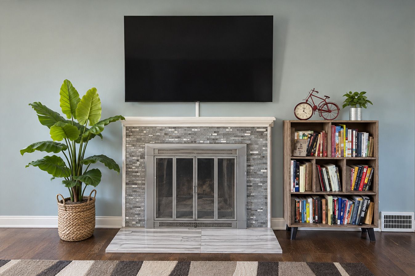 A living room with a fireplace, a flat-screen TV mounted above it, a bookshelf filled with books, a potted plant, and a bicycle.