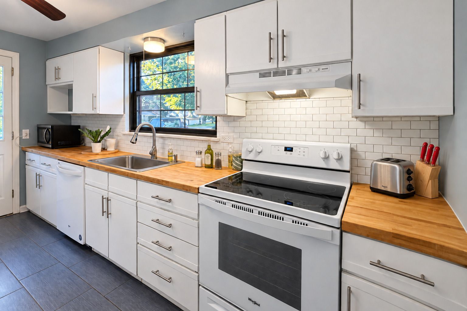 A modern kitchen with white cabinets, a stainless steel sink, a built-in oven, and a toaster.
