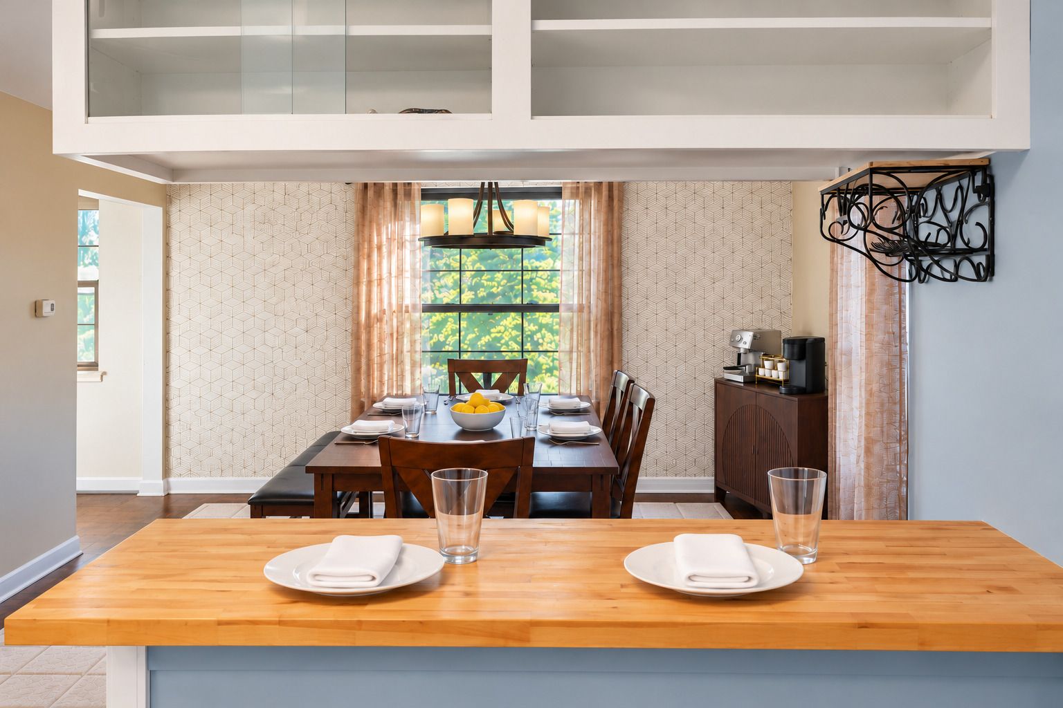 A dining area with a wooden table, chairs, and a view of greenery through a window.