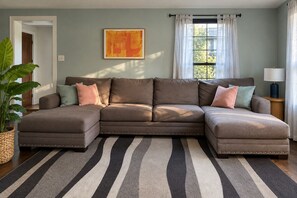 Un sofá modular con un tapete a rayas, una obra de arte enmarcada en la pared y una ventana con cortinas.