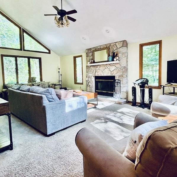 A living room with a stone fireplace, a large sofa, and a television. - Charming 4-Bedroom Cabin in Lake Harmony, PA PERFECT for your next getaway! (Lake Harmony)