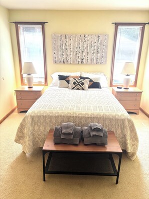 A bedroom with a bed, two nightstands, a bench with towels, and a wall art piece. - Charming 4-Bedroom Cabin in Lake Harmony, PA PERFECT for your next getaway! (Lake Harmony)