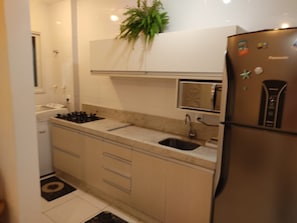 A compact kitchen with a built-in microwave, a stainless steel refrigerator, and a sink. - Apartamento Completo Praia Canasvieiras (Florianópolis)