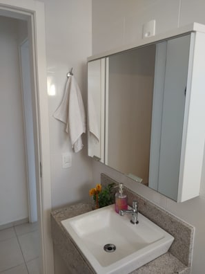 A bathroom with a white sink, a mirror, and a towel hanging on the wall. - porto caravelas (Florianópolis)