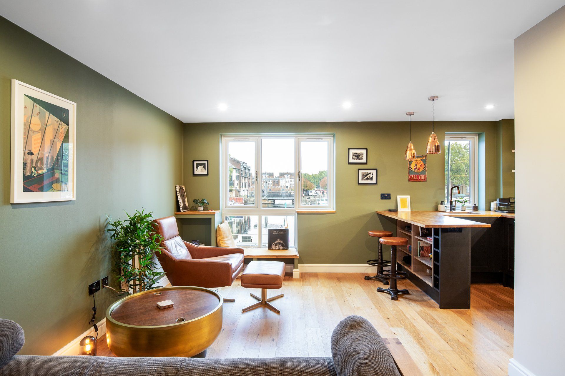 Un salon moderne avec un canapé en cuir marron, une table basse ronde et une vue sur le paysage urbain, visible à travers de grandes fenêtres.