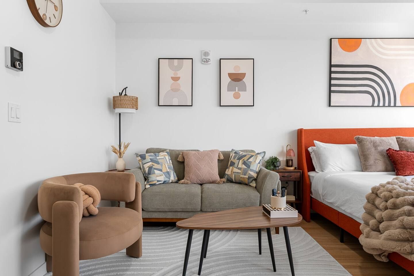 Uma sala de estar moderna com sofá, poltrona e cama com cabeceira laranja.