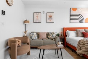 Una sala moderna con un sofá, un sillón y una cama con cabecera naranja.