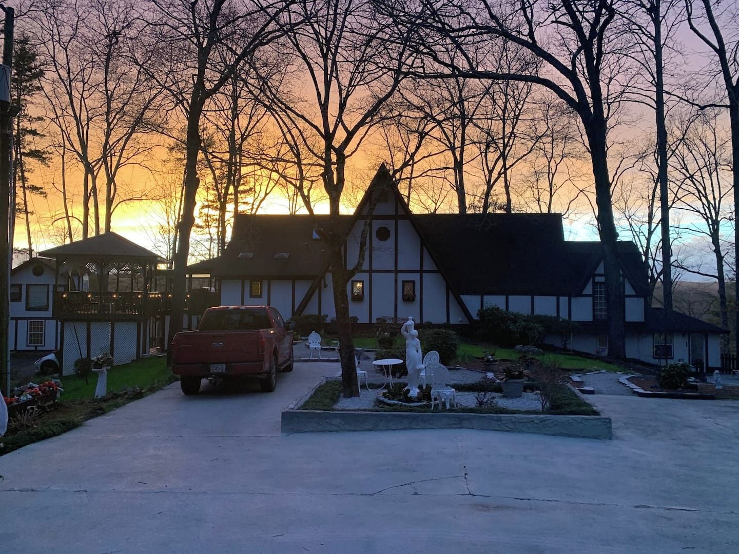 A house with a driveway, a red truck parked in front, and a garden with a statue.