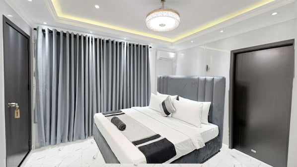 A modern bedroom with a large bed, a headboard, and a ceiling light fixture. - Suisse Luxury Residence (Nallur)