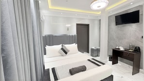 A modern bedroom with a bed, bedside table, and a TV mounted on the wall. - Suisse Luxury Residence (Nallur)