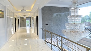A spacious hallway with a marble floor, a grand chandelier, and a view of greenery outside. - Suisse Luxury Residence (Nallur)