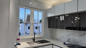 A modern kitchen with a window, a sink, and a marble backsplash. - Suisse Luxury Residence (Nallur)
