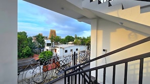 A balcony with a view of a building with a tower, surrounded by greenery and other structures. - Suisse Luxury Residence (Nallur)