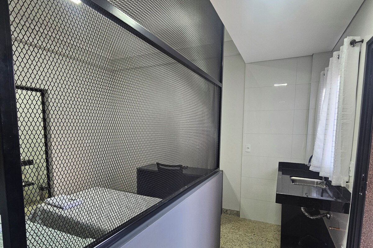 A modern bathroom with a shower, a sink, and a toilet. There is a partition with a mesh design.