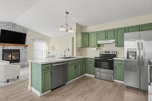 A modern kitchen with green cabinets, a stainless steel refrigerator, a built-in oven, and a fireplace.
