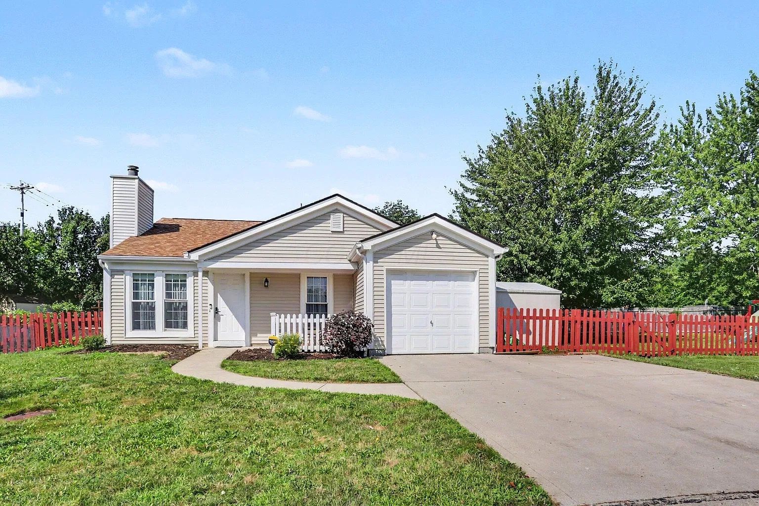 A single-story house with a garage, a front porch, and a red picket fence.