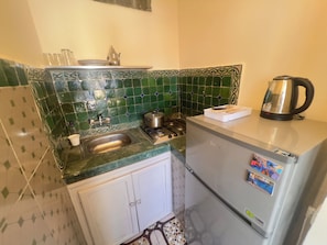 A compact kitchen with a sink, stove, and refrigerator, featuring green patterned tiles and a stainless steel kettle. - BLUE CITY (Chefchaouen)