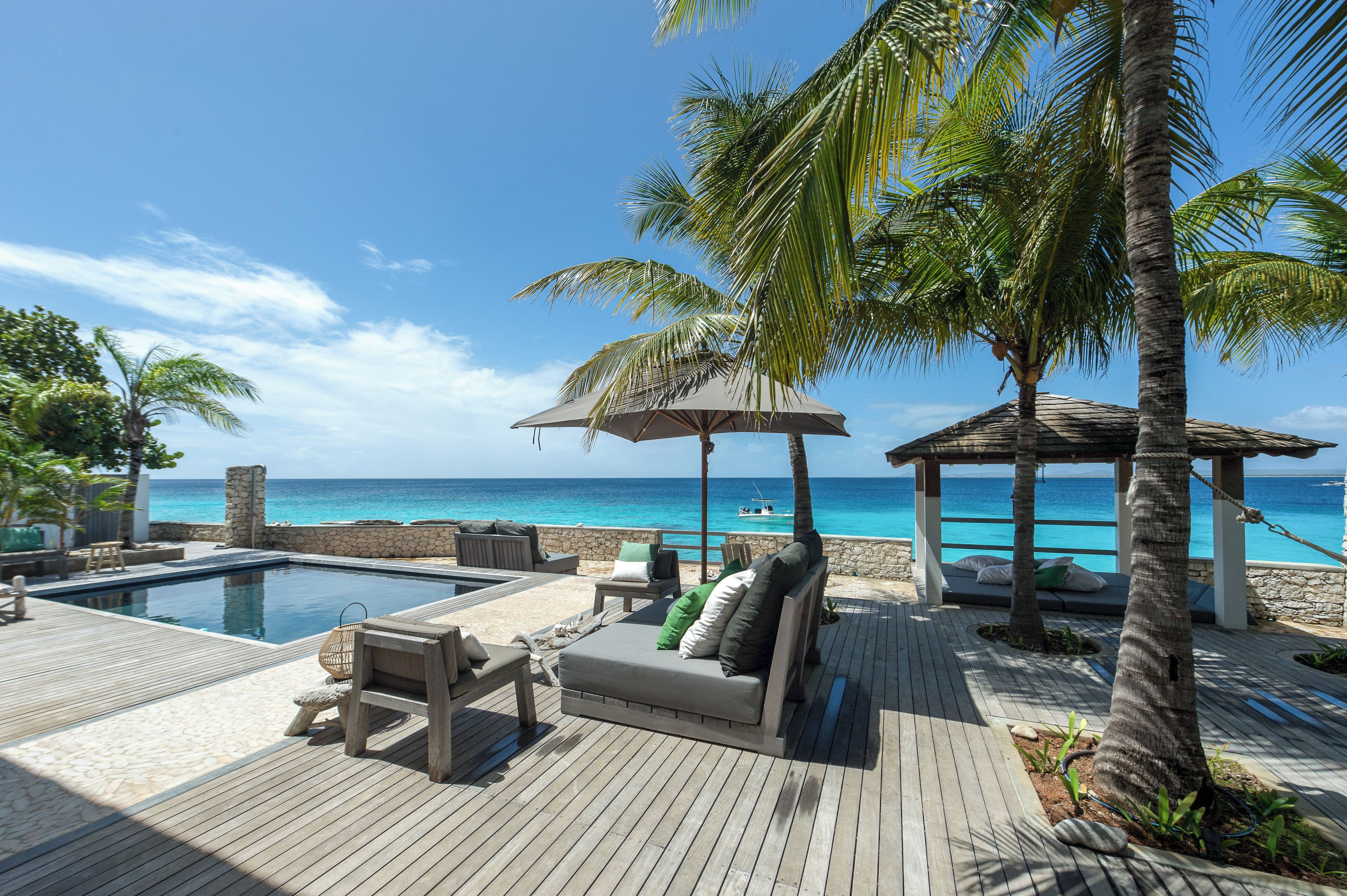 A wooden deck with a pool, lounge chairs, and a gazebo overlooking the ocean.
