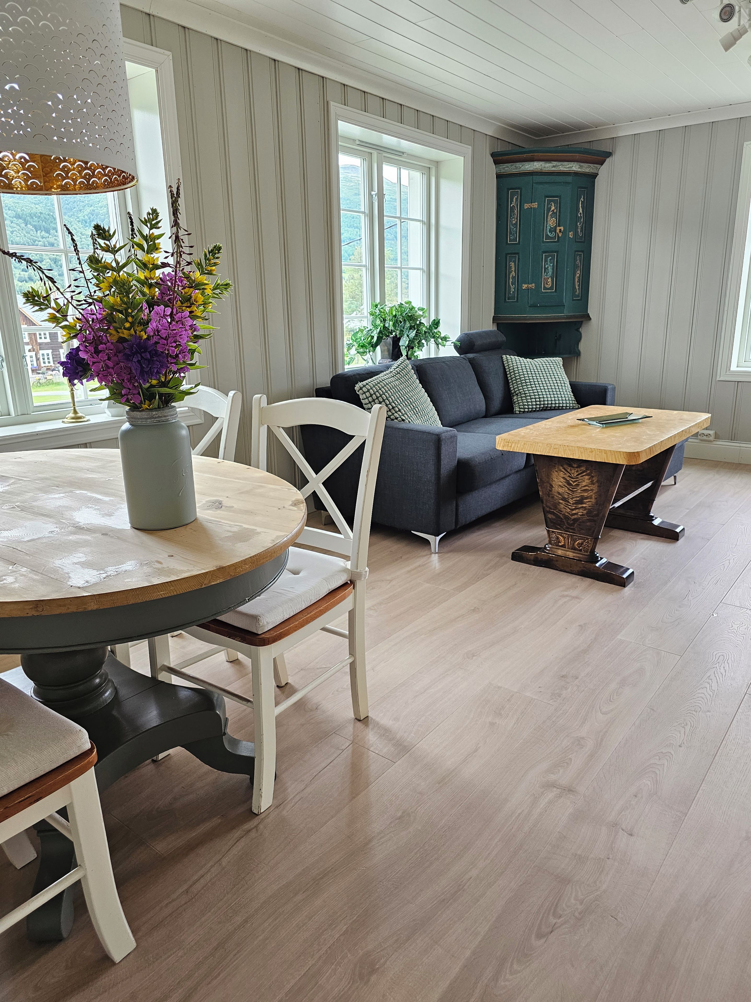 A room with a dining table, chairs, a sofa, a cabinet, and a window with a view.