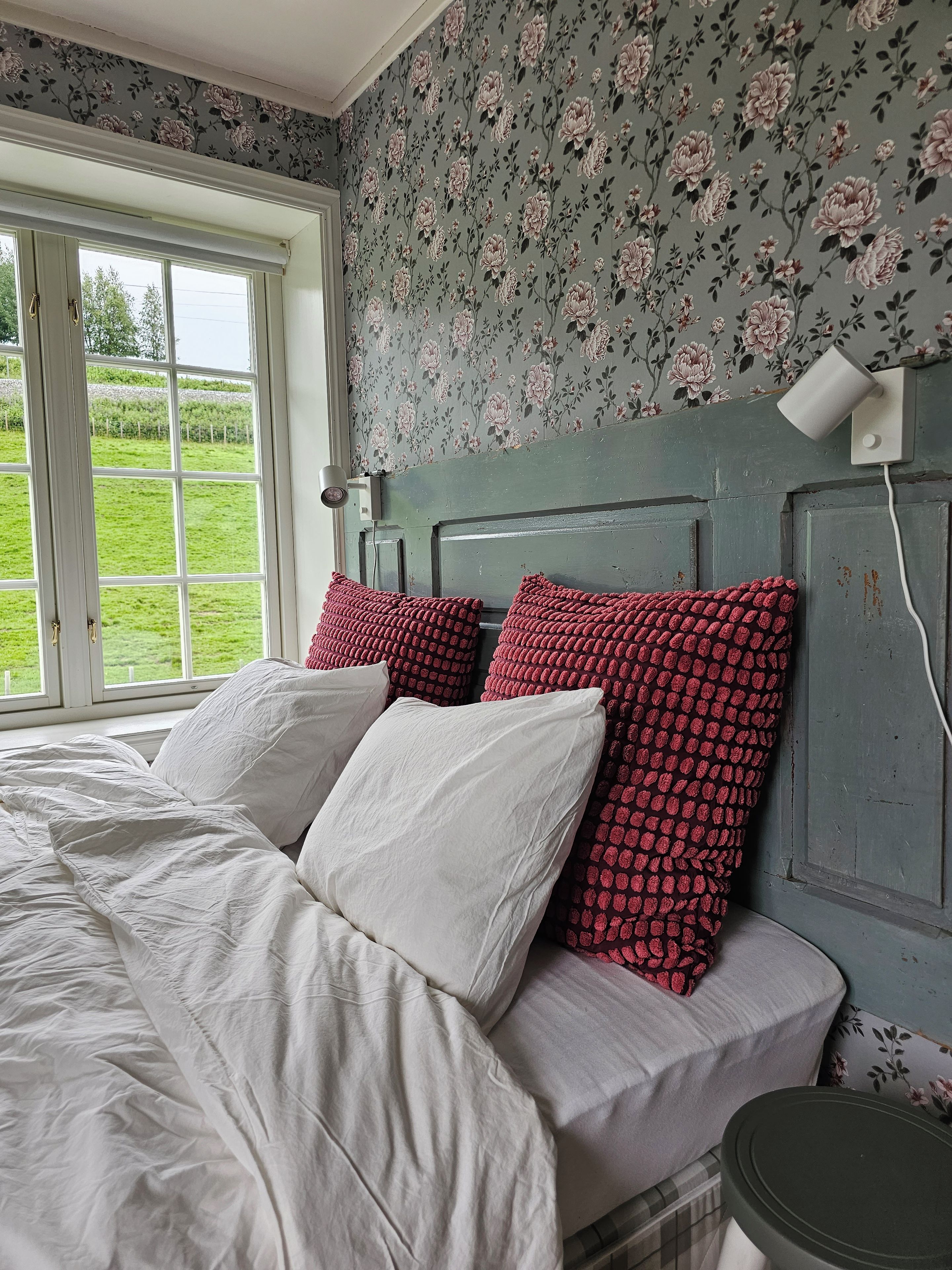 A bedroom with a bed, pillows, a headboard, a window, and a lamp.