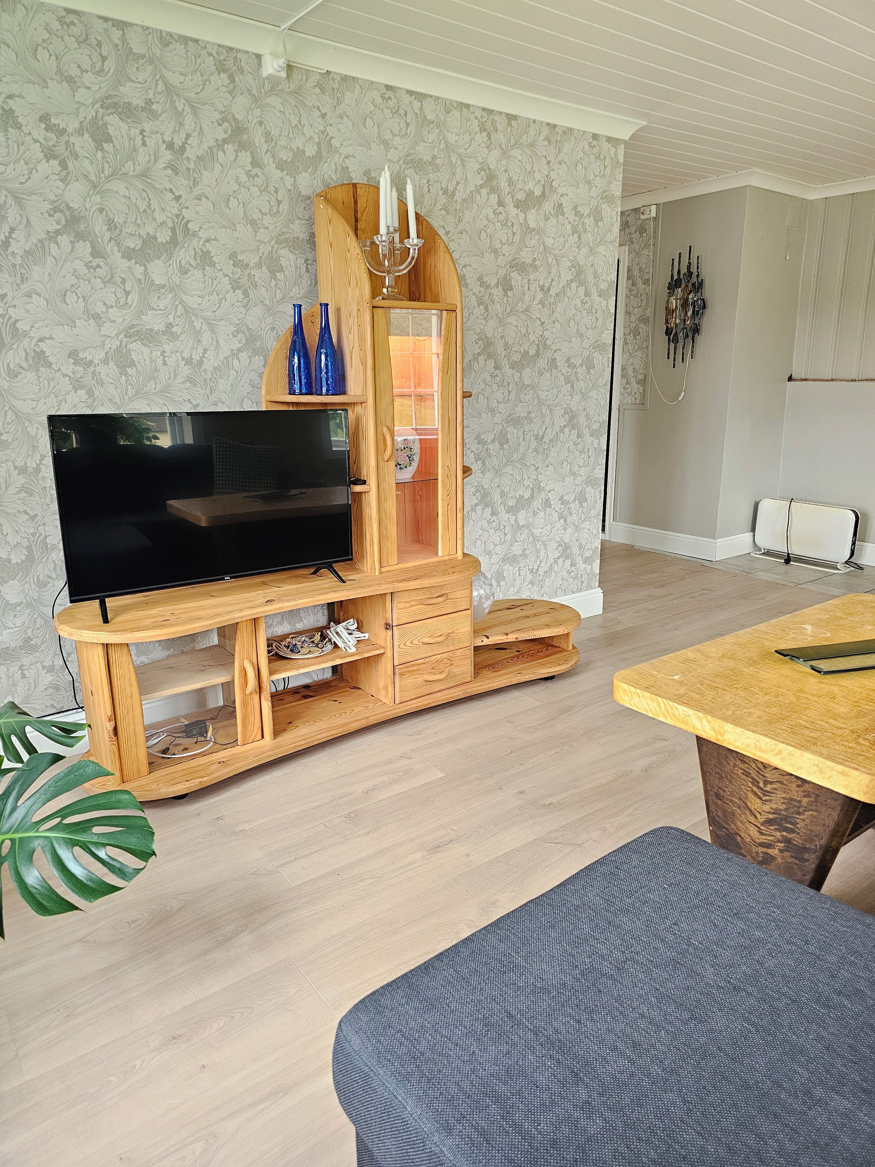 A living room with a wooden entertainment center, a flat-screen TV, and a dining area with a table and bench.