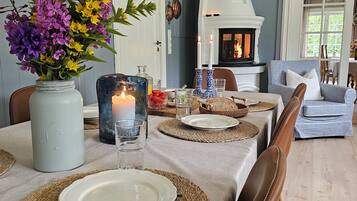 Un comedor con una mesa lista para dos personas, con individuales tejidos, platos blancos y un jarrón con flores.