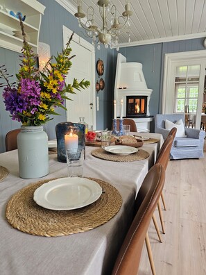 Un comedor con una mesa lista para dos personas, con individuales tejidos, platos blancos y un jarrón con flores.