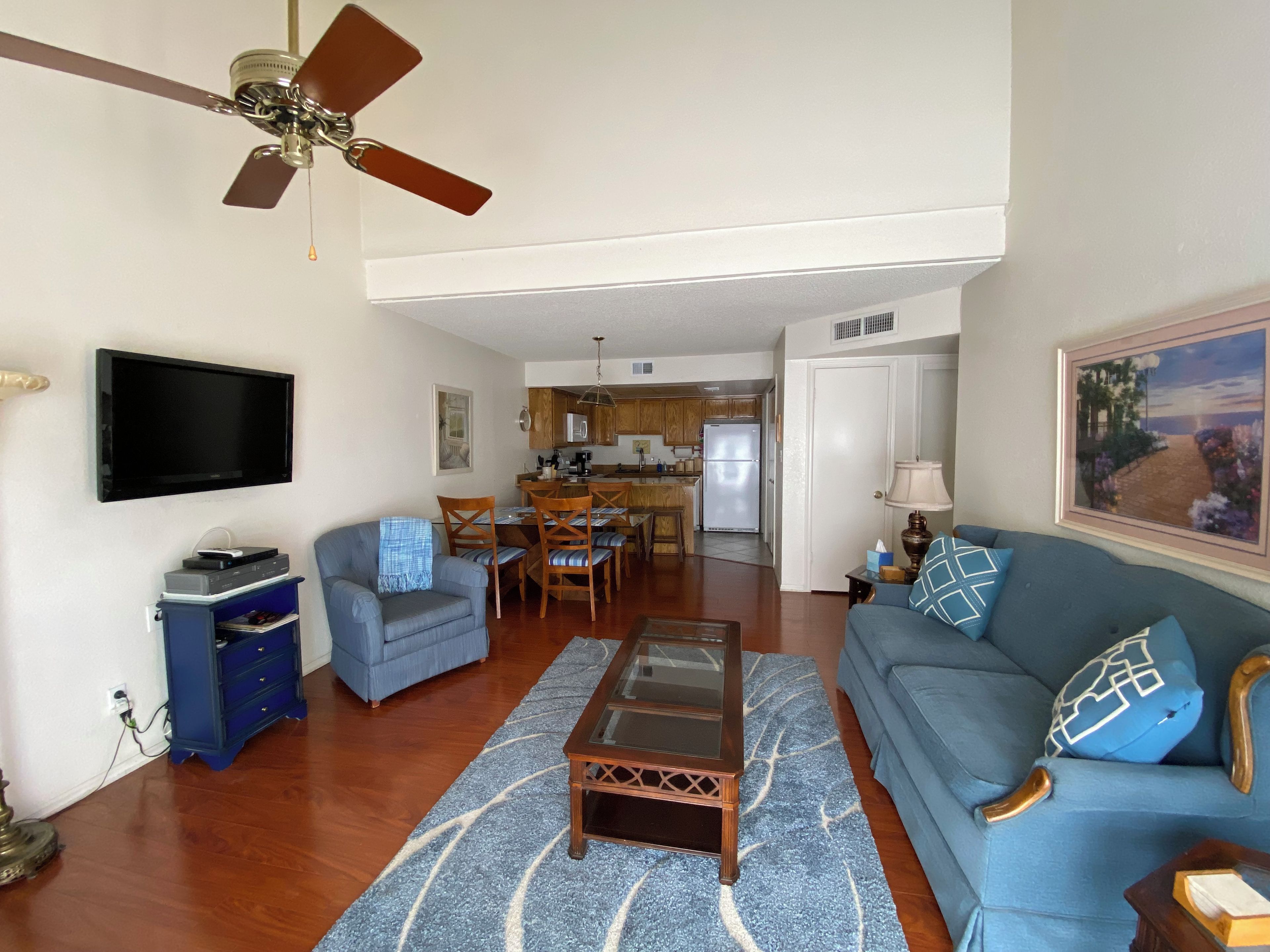 A living room with a sofa, armchair, coffee table, and a TV mounted on the wall.