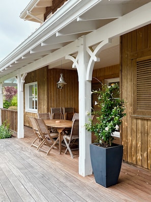 A covered outdoor patio with a wooden table and chairs, a potted plant, and a white railing. - New Listing (La Teste-de-Buch)