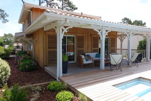 Ein Holzhaus mit überdachter Terrasse, Sitzgelegenheiten im Freien und einem Swimmingpool.